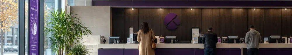Modern retail bank branch interior, a teller line with two or three customers seen from behind